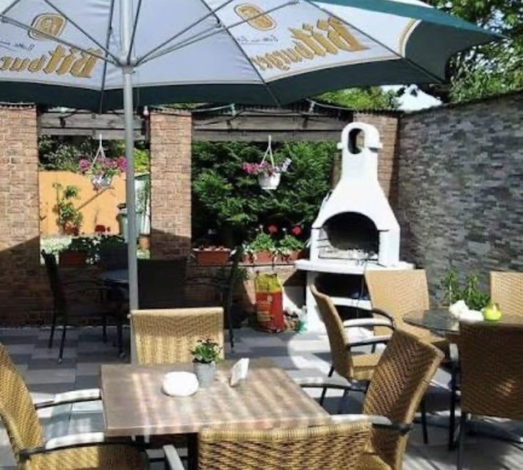 Gemütlicher Gartenbereich mit Tisch, Stühlen und einem Grill unter einem Sonnenschirm.